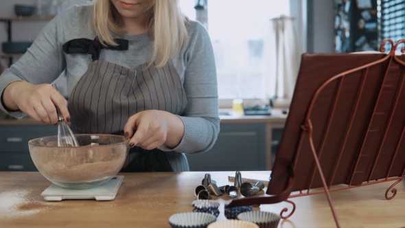 Young Beautiful Woman Mixing Ingredients in Bowl, Using Whisk Attractive Female Looking at Recipe