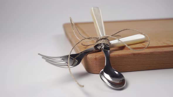 Shiny spoon and fork tied with jute on a wooden board and a white surface
