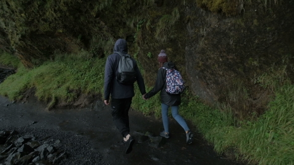 A Couple Hikers Hiking with Backpacks Walk Along a Beautiful Mountain Area Holding Hands