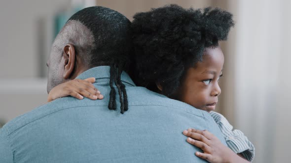 Happy African American Kid Girl Hugging Beloved Father Unrecognizable Adult Man Sits with Back to