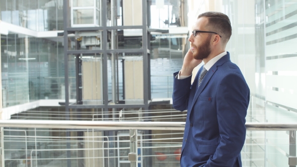 Young Businessman Uses Smartphone, Standing in Business Center.