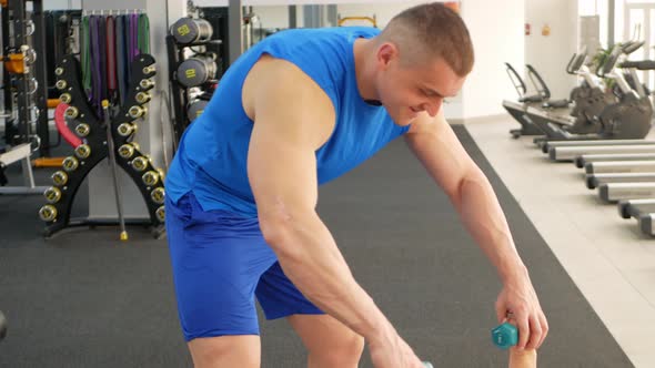 Pensioner Performs an Exercise with Dumbbells on Mat in Gym