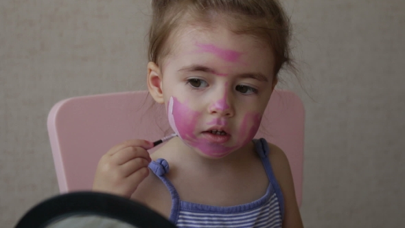 Blonde Three Years Old Baby Painting Color Stripes on Her Face Looking at Mirror