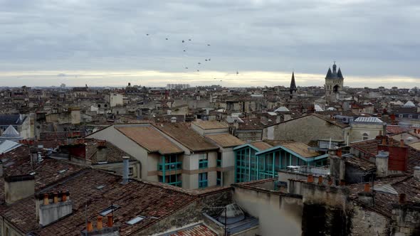 French city of Bordeaux rooftops showing Cailhau City Gate and pigeon flocks flying, Aerial pan righ