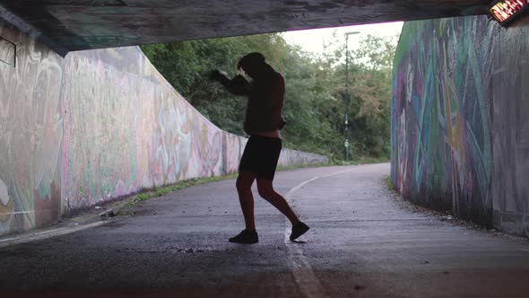 Wide Shot of a Young Athletic Man Boxing in an Underpass, Silhouetted By The Light Behind Him