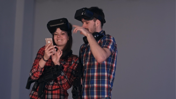 Laughing Couple in Virtual Reality Headsets Looking at Their Funny Photos on the Phone