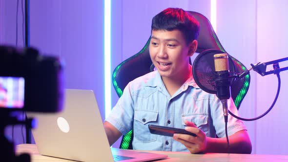 Asian Kid Boy Holding Phone And Read Comment In Laptop Then Talking To Camera While Live Stream