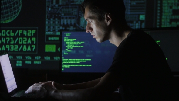 Portrait of a Young Programmer Working at a Computer in the Data Center Filled with Display Screens