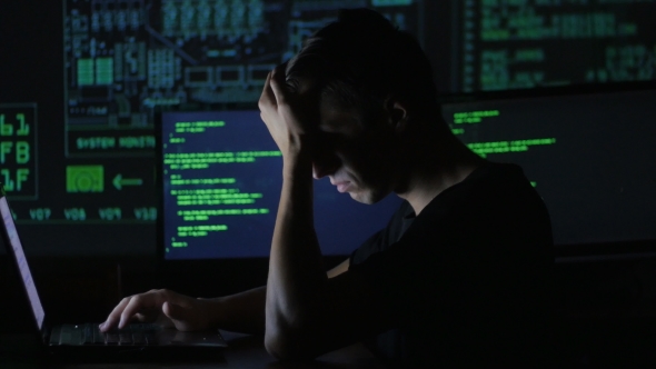 Portrait of Tired Young Programmer Working at a Computer in the Data Center Filled with Display