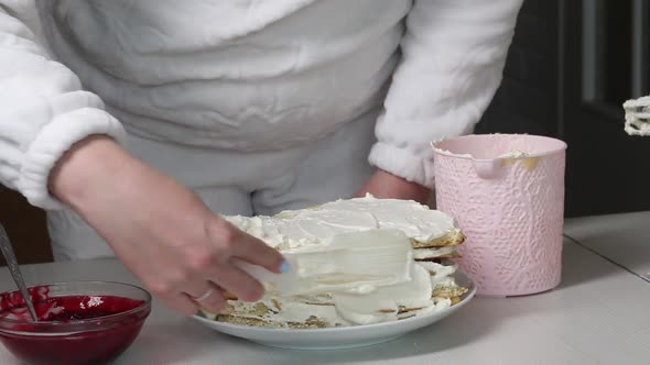 A Woman Smears A Biscuit Cake With Cream. Nearby Is A Container With Cherry Filling For The Cake