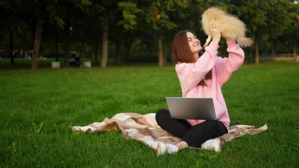 A Small Dog Interferes with a Girl in the Park with a Laptop to Study or Work