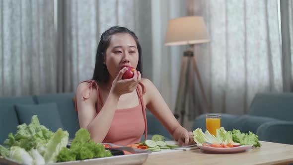 Happy Asian Woman Biting An Apple While Having Healthy Food At Home
