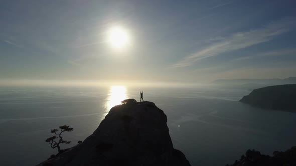 Aerial Silhouette of Young Woman Standing on the Top of a Mountain Facing the Sea