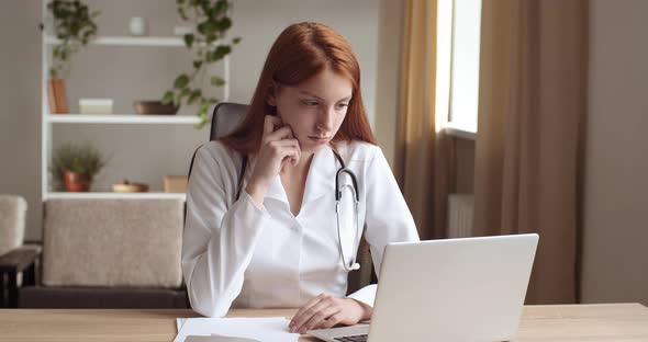 Concentrated Young Professional General Practitioner Woman in White Uniform Looking at Laptop Screen