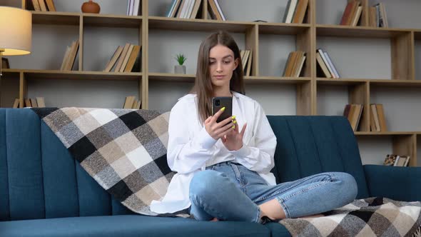 Happy Young Woman Using Mobile Phone While Sitting a Couch at Home