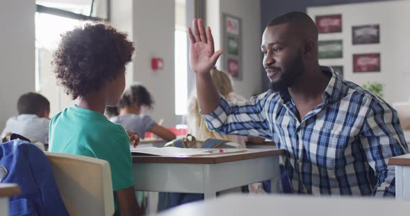 Video of happy african american male teacher clapping hands with african american boy alt