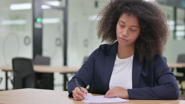 Serious Young African Businesswoman Writing on Paper