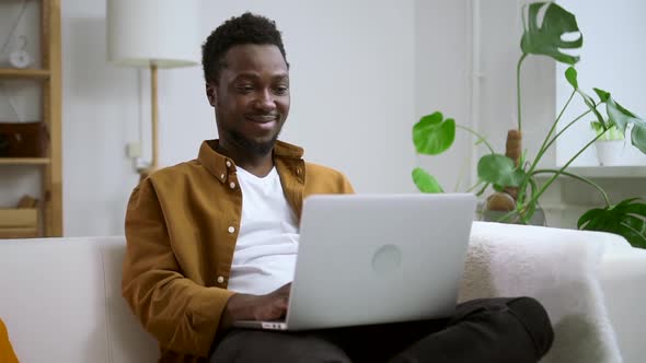 Man Using Laptop and Smiling Sitting on Couch at Home Room During Pandemic Spbas