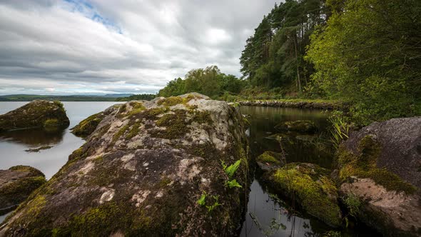 Panorama motion time lapse of lake with large rocks in the foreground and forest in the distance on