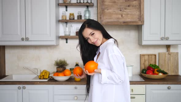 Happy Young Female Playing With Orange In Kitchen