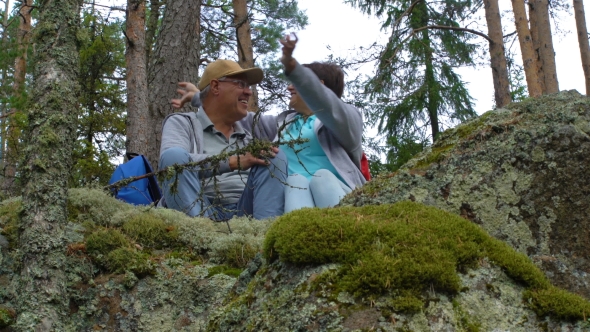 Elderly Active Couple Sitting on a Rock and Admiring the Northern Forest