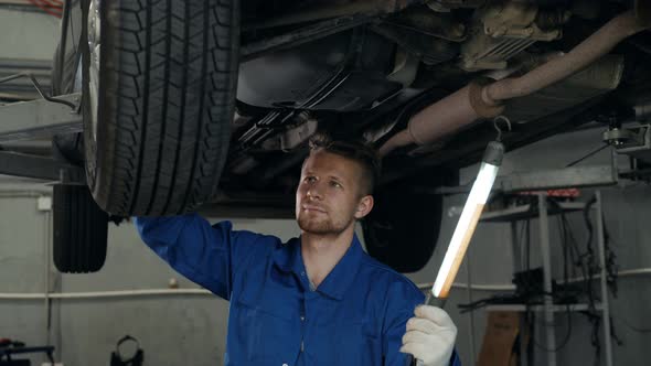 Car Mechanic Examining Car Suspension of Lifted Automobile at Repair Service Station with Light