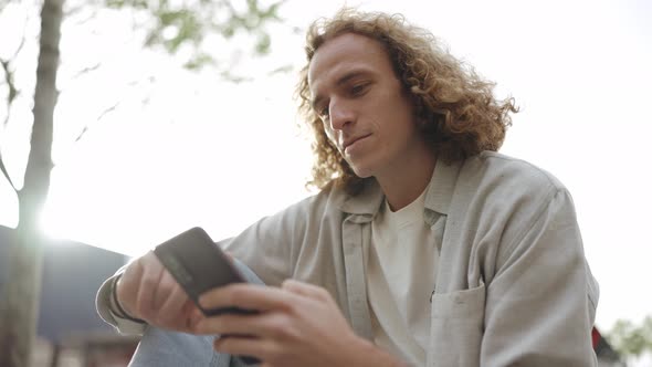 Handsome curly-haired man typing by phone