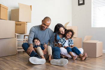 ome. Young multiethnic parents with two sons in their new house with cardboard boxes. Smiling little boys sitting on floor with mother and dad.