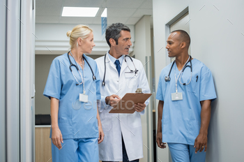n a hallway hospital. Doctor discussing patient case status with his medical staff after operation. Doctor holding clipboard while in conversation with nurse.