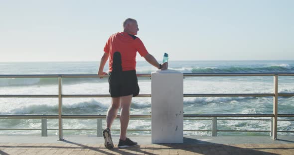 Senior man holding water bottle standing on the promenade