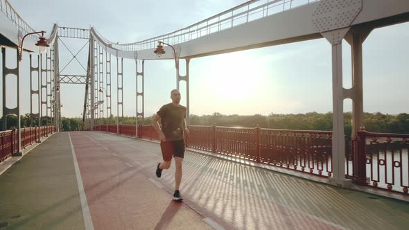 Athletic Young Man Runs on Pedestrian Bridge in the City at Dawn