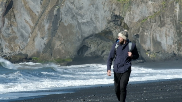 Man with a Backpack, Walking Along the Shore of Black Sand Beach in Iceland