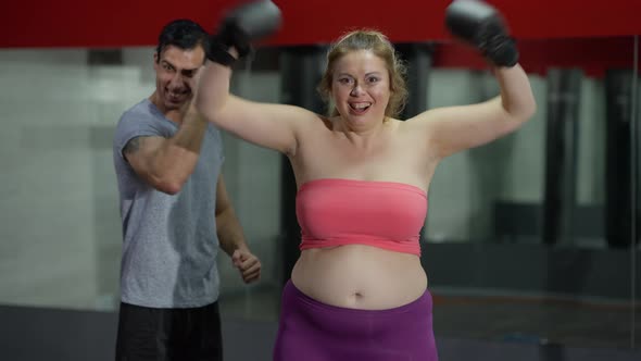 Portrait of Cheerful Excited Overweight Woman in Boxing Gloves Gesturing Victory with Smiling Man