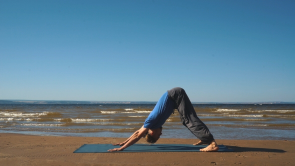 Young Man Standing in the Downward Facing Dog Position on the Beach