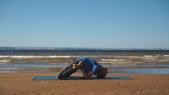 Strong Man Practicing Difficult Yoga Pose on the Beach