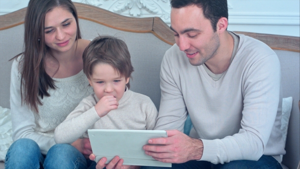 Dad, Mom and Their Young Son Having Fun By Playing Together with a Tablet Sitting on a Couch