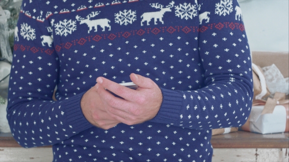 Young Man in Christmas Knitwear Holding Phone in His Hands