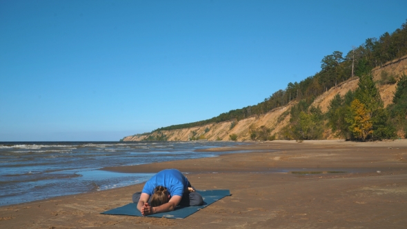 Young Man Doing Thoracic Stretching on a Beach at Sunset Light