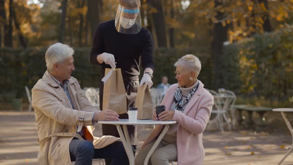 Smiling Senior Couple Sitting at Cafe and Receiving Takeaway Order