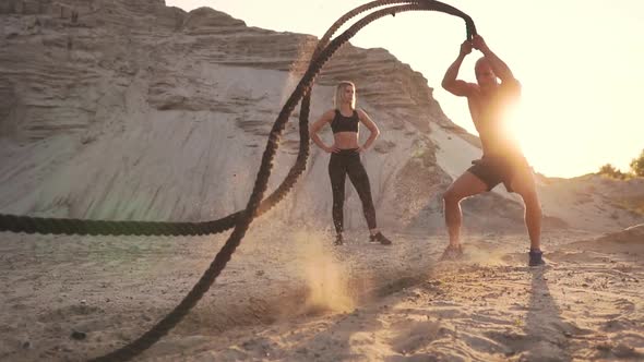 Athletic Man on Exercise Around the Sand Hills at Sunset Hits the Rope on the Ground and Raised the