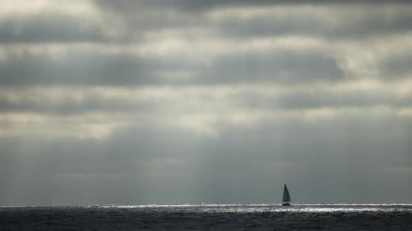 A lonely sailboat on a voyage during dark skies and stormy weather in the vast ocean