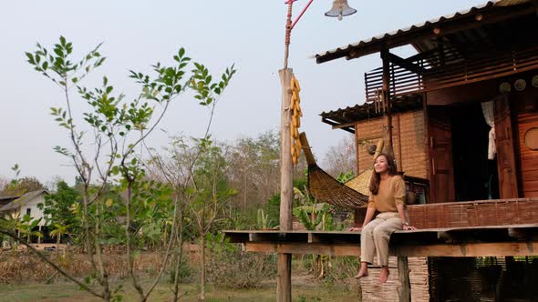 A woman sitting and chilling on wooden house balcony with nature view in countryside