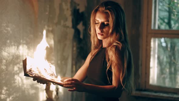 Beautiful Young Woman in a Black Dress Is Holding a Burning Old Book in Her Hands at a Vintage Old