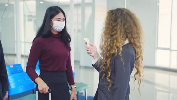 Caucasian female airline staff measure body temperature of passenger before entering the airport.