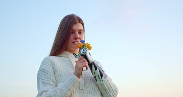 a Smiling Woman with a Bionic Hand Sniffs a Bouquet of Wild Flowers