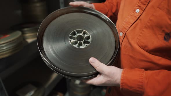 A man opens an old metal round box with an old film strip inside