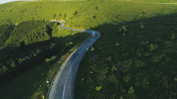 Semi Truck Driving on Asphalt Road in a Rural Landscape with Green Forested Hills