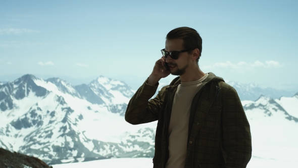 Young Bearded Man Talking on Mobile Phone at Snowy Mountains with Scenic View