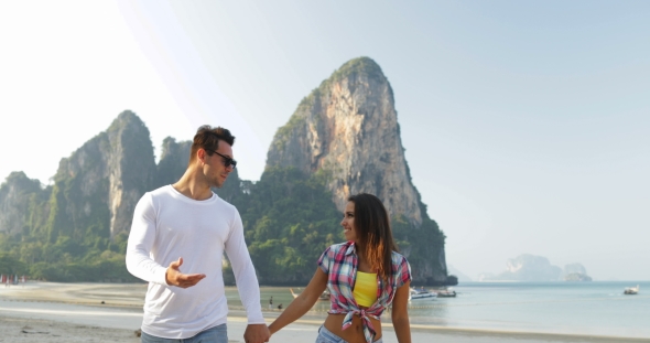 Couple Walking On Beach Holding Hands Talking Young Man And Woman Tourists On Vacation