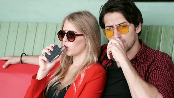 Stylish Couple in a City. Two People Use the Electronic Cigarette